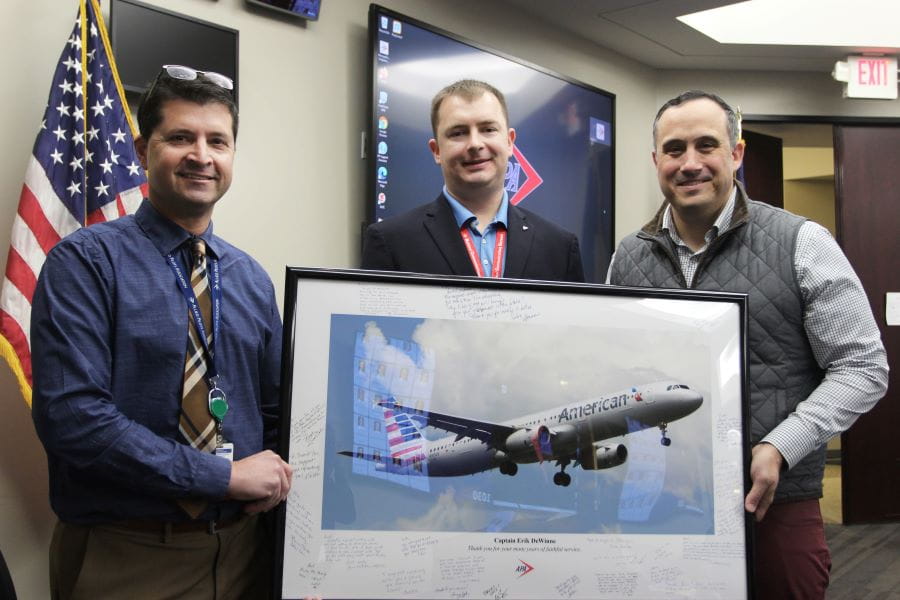 three men, one of whom is holding a framed print of a plane