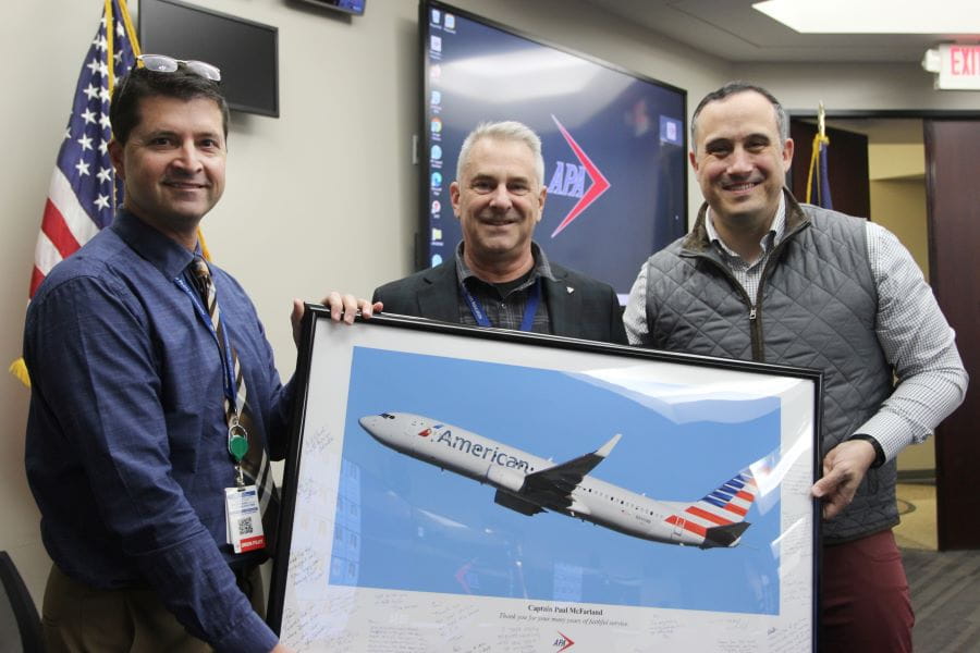 three men, one of whom is holding a framed print of a plane