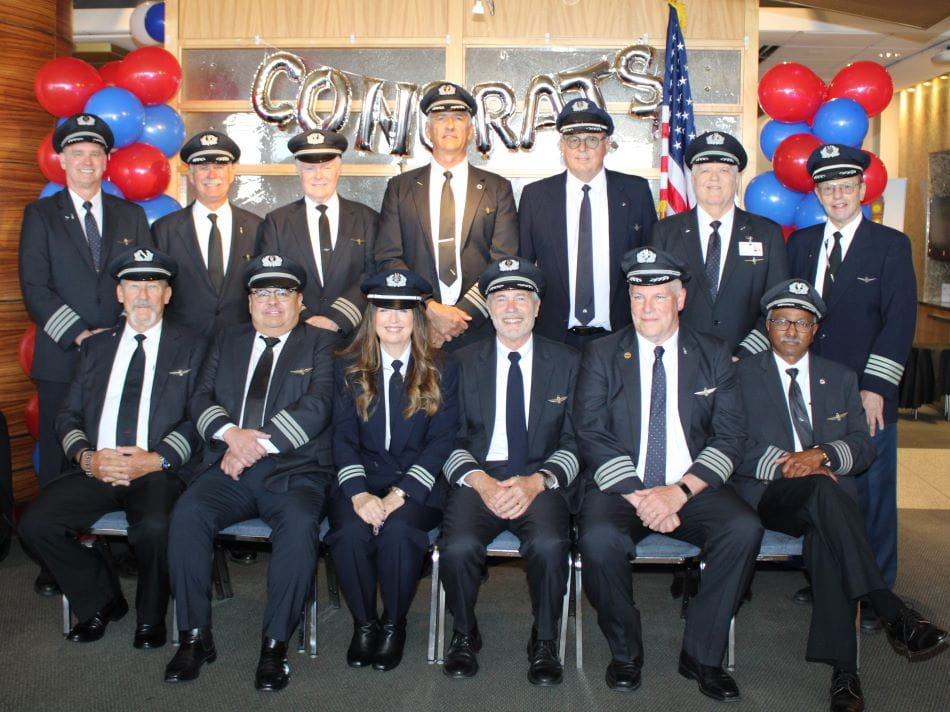 a group of 13 pilots in uniform under 'congratulations' ballons