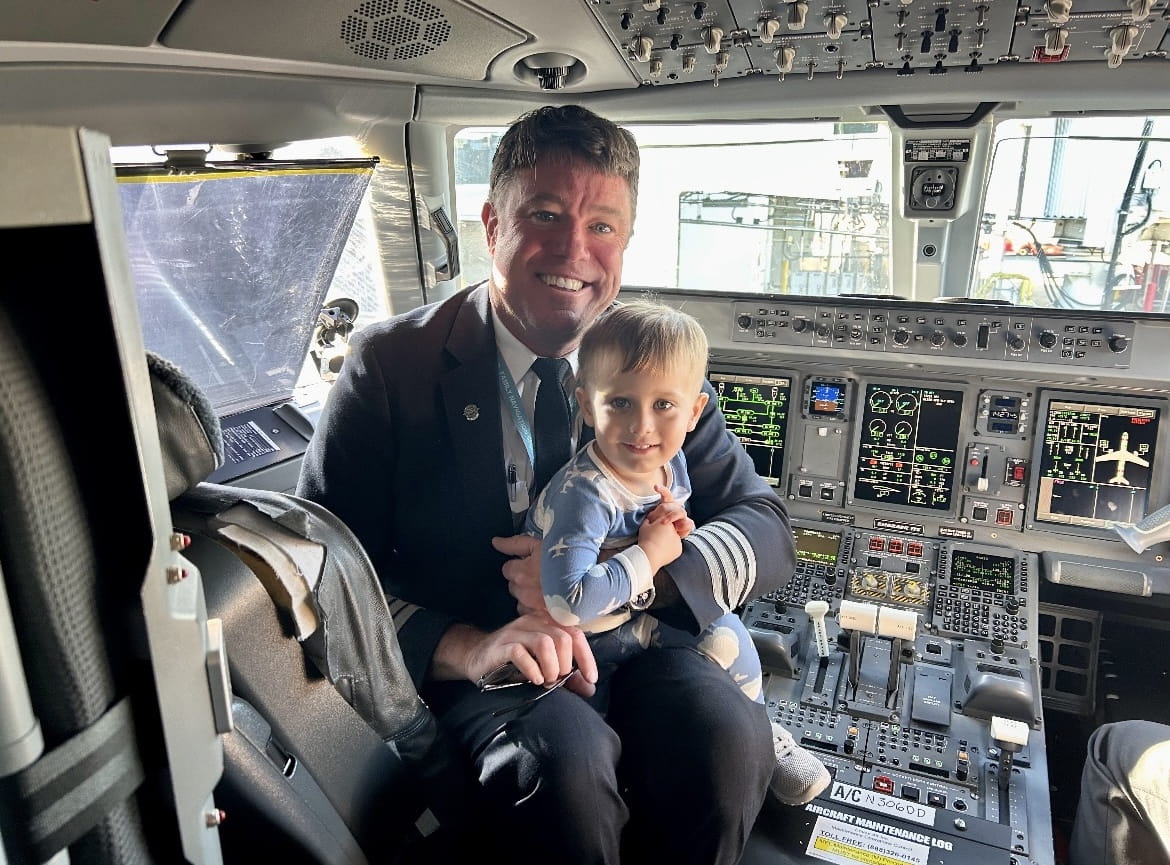 a pilot in a cockpit with a young boy in his lap